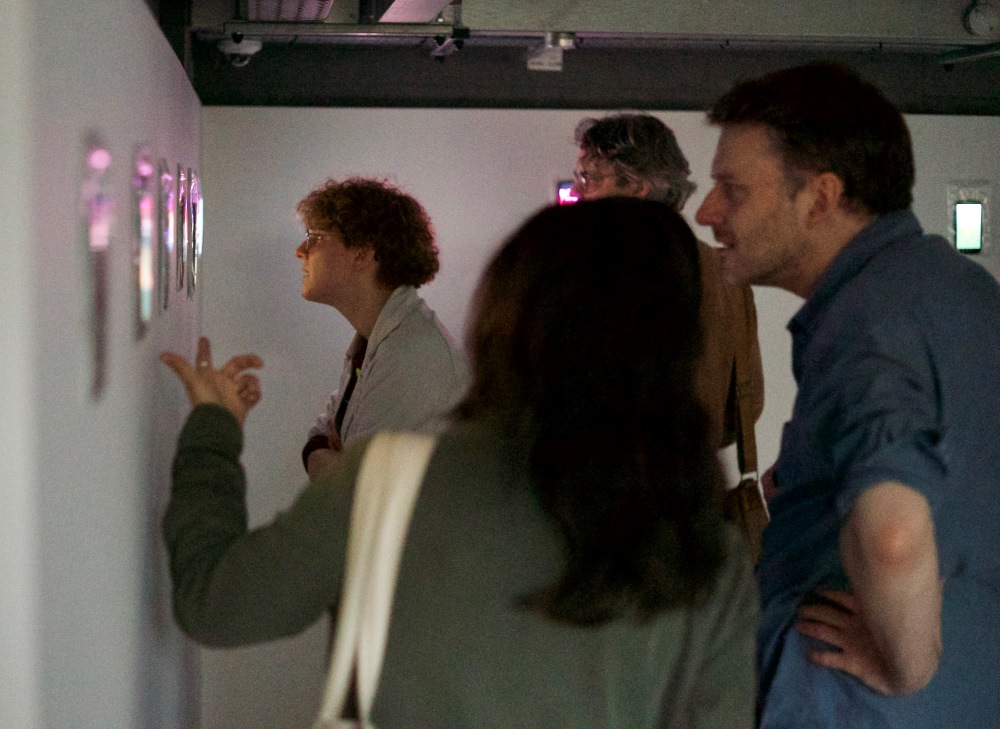 Install shot from 100 Videos event showing people viewing videos works mounted on walls.