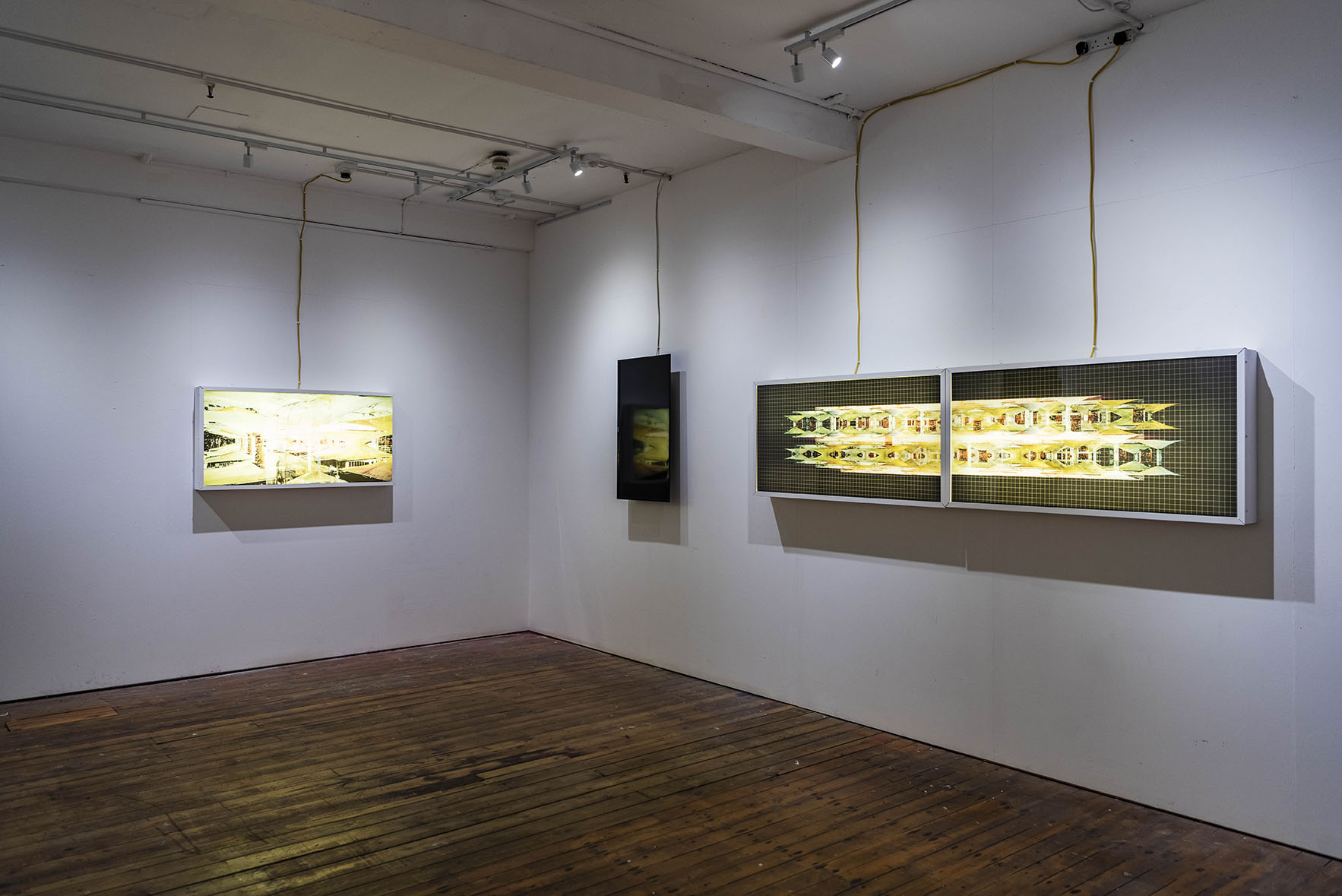 Screens showing a yellow image on a white gallery wall