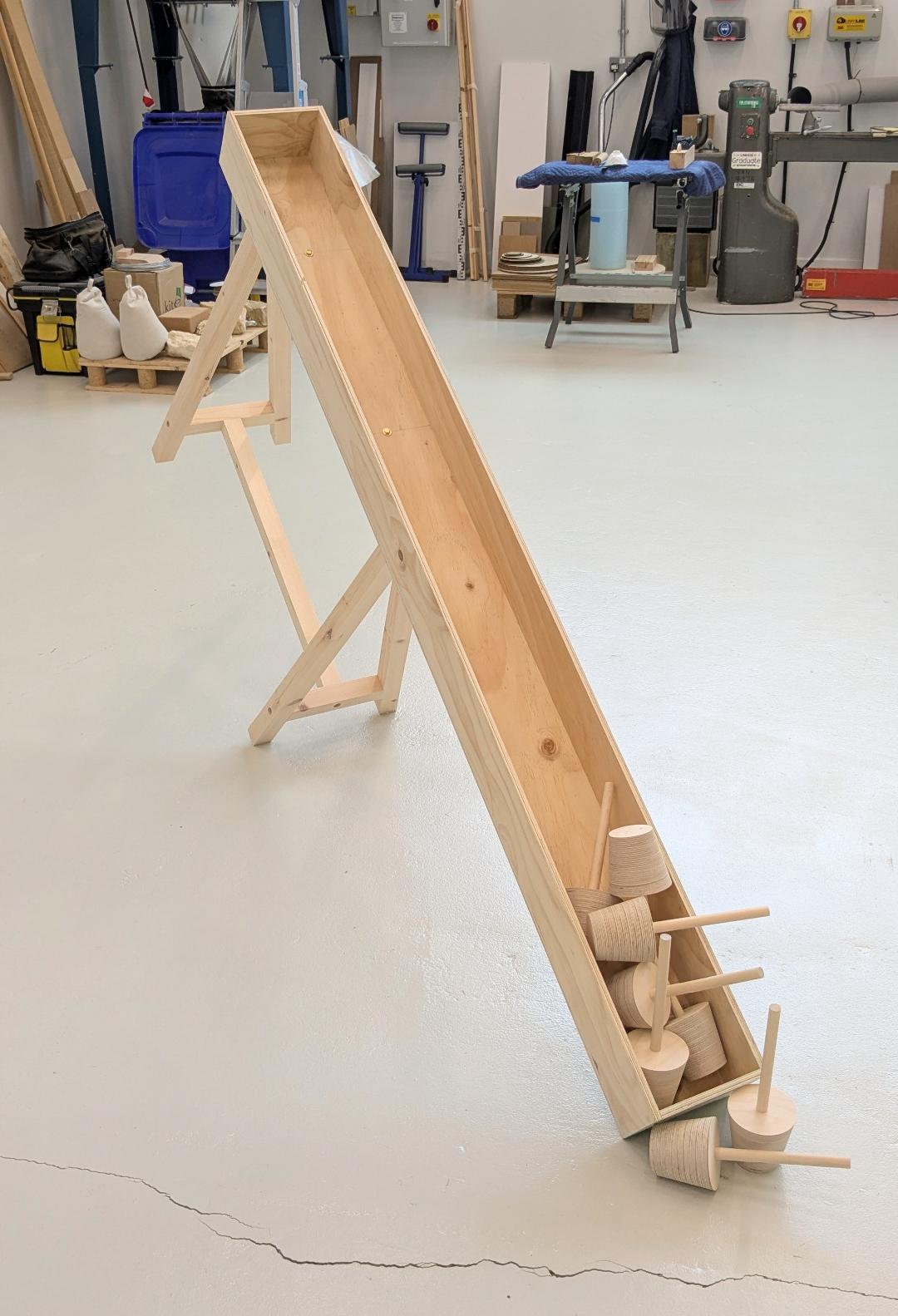 A wooden sculpture in the shape of a slide, with small wooden sculptures at the bottom