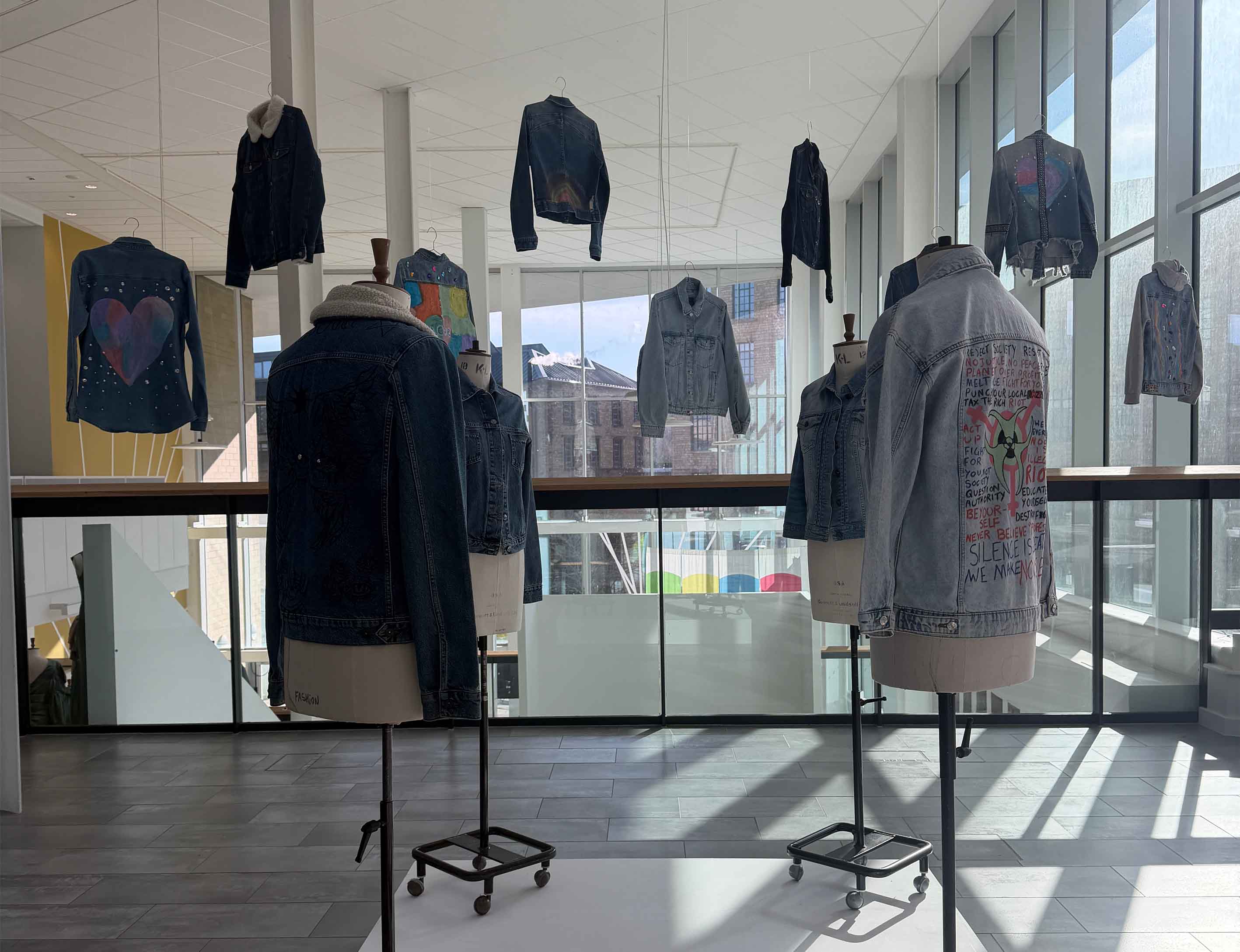 4 mannequins with customised denim jackets on, with some denim jackets suspended in the background.
