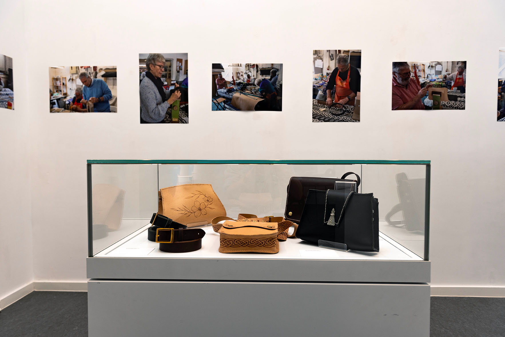 Photographs on a wall and leather items in a glass case