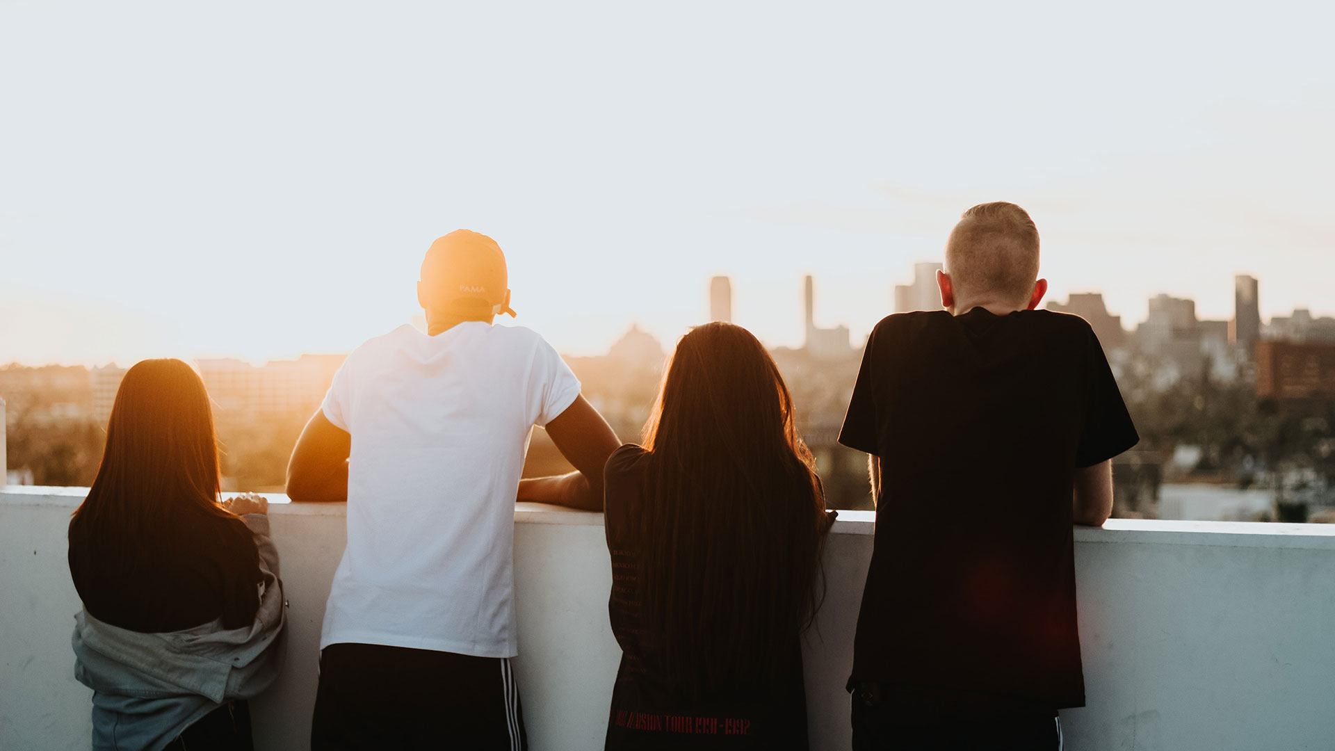 The back of four young people looking off a balcony into the sunrise