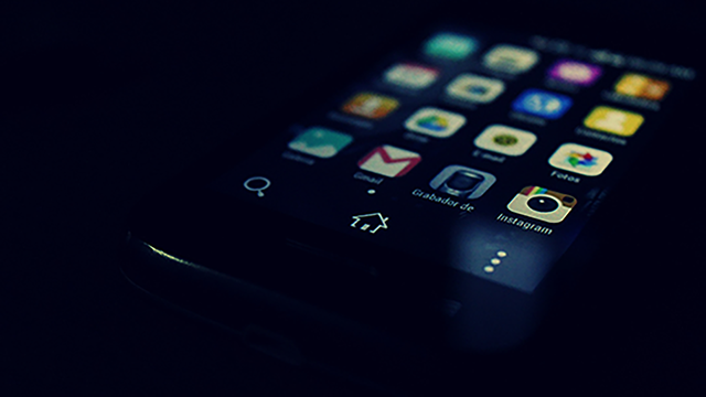 A phone screen in a darkened room showing a number of apps
