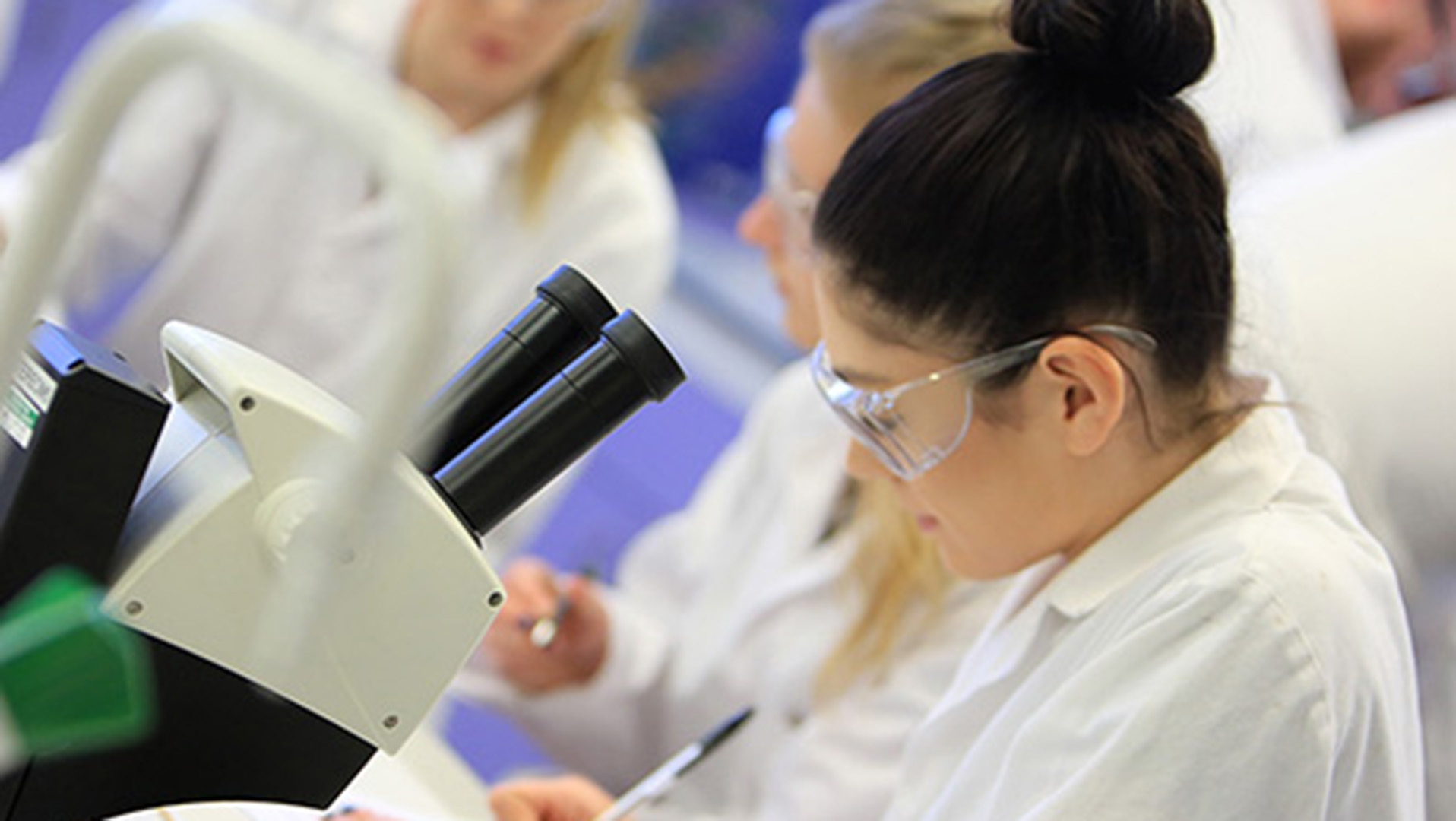 Female researcher in a lab recording data from a microscope