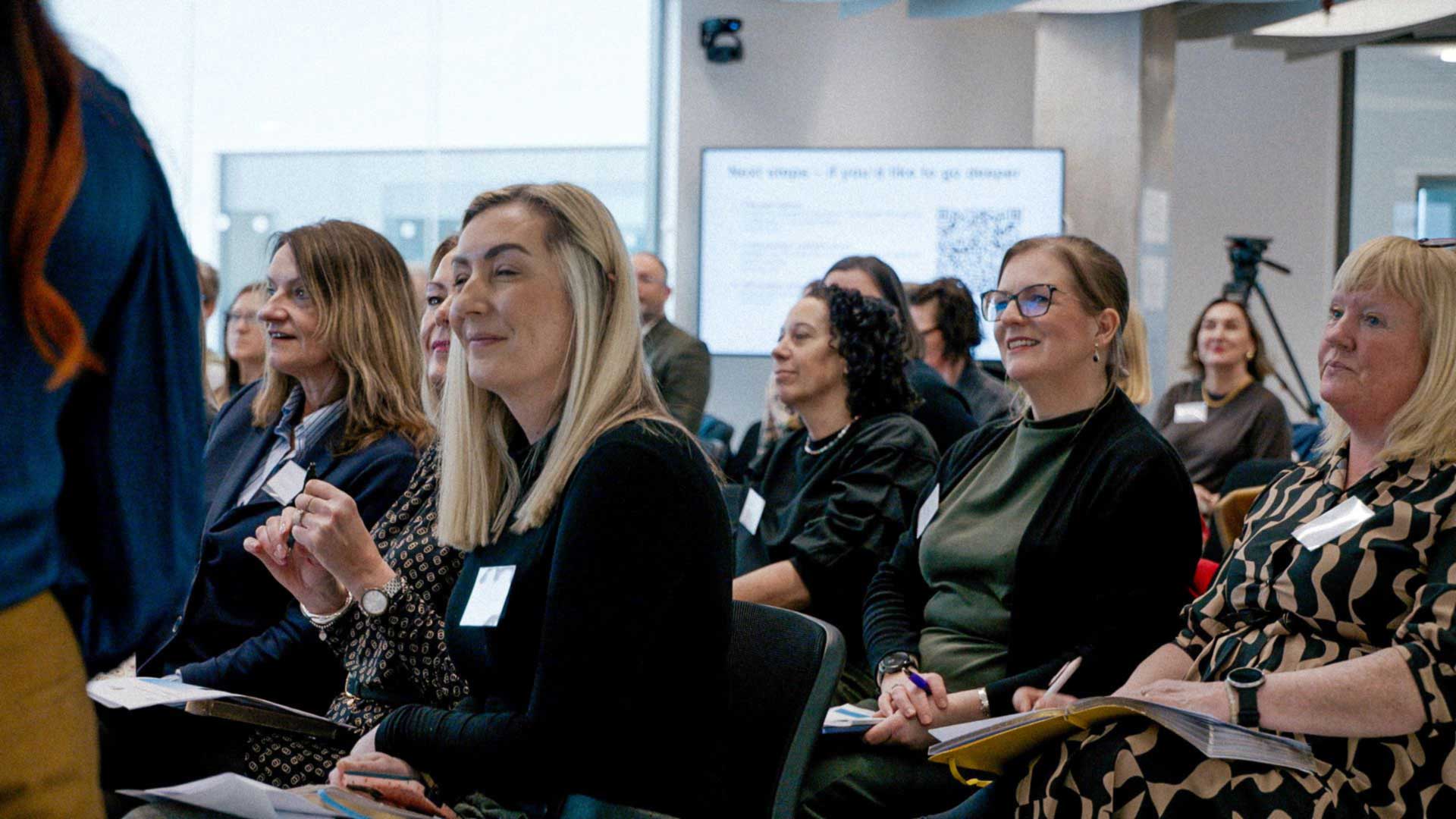 A number of people sat on chairs in rows, looking forward and listening.