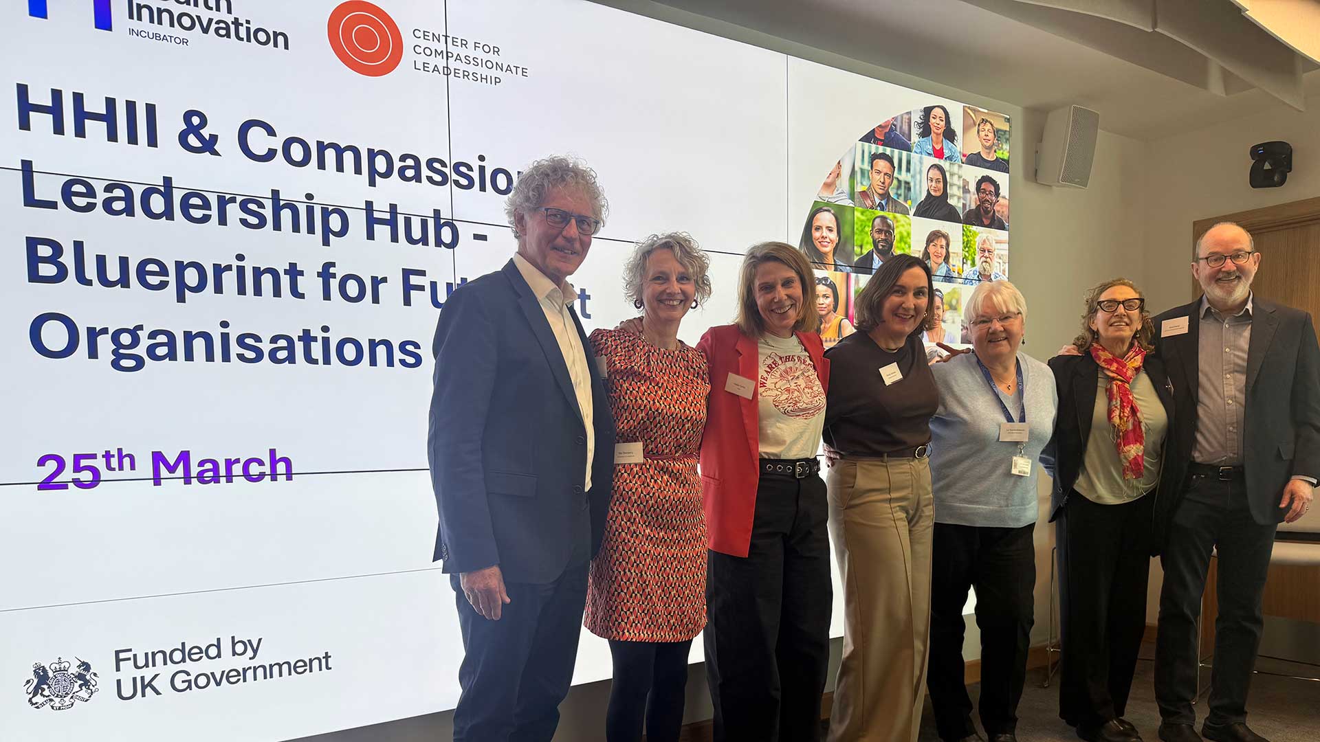 A group of people stand in line in front of a presentation for the Compassionate Leadership Hub