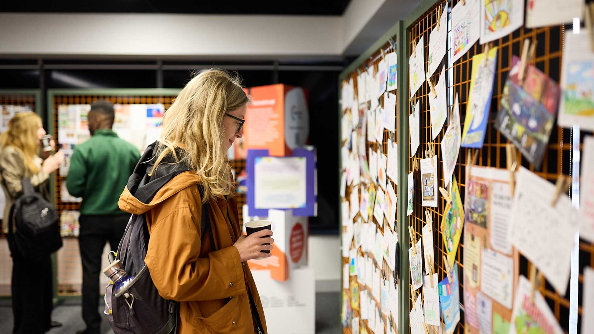 Picture of woman in yellow jacket looking at a wall of pictures